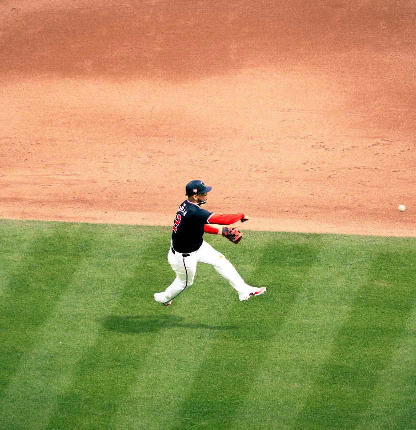 Infielder in a navy and red uniform throwing across the diamond, the ball in flight over the outfield grass