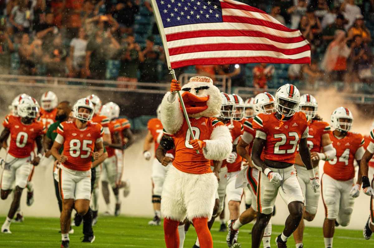 Miami Hurricanes taking the field behind the mascot carrying the American flag