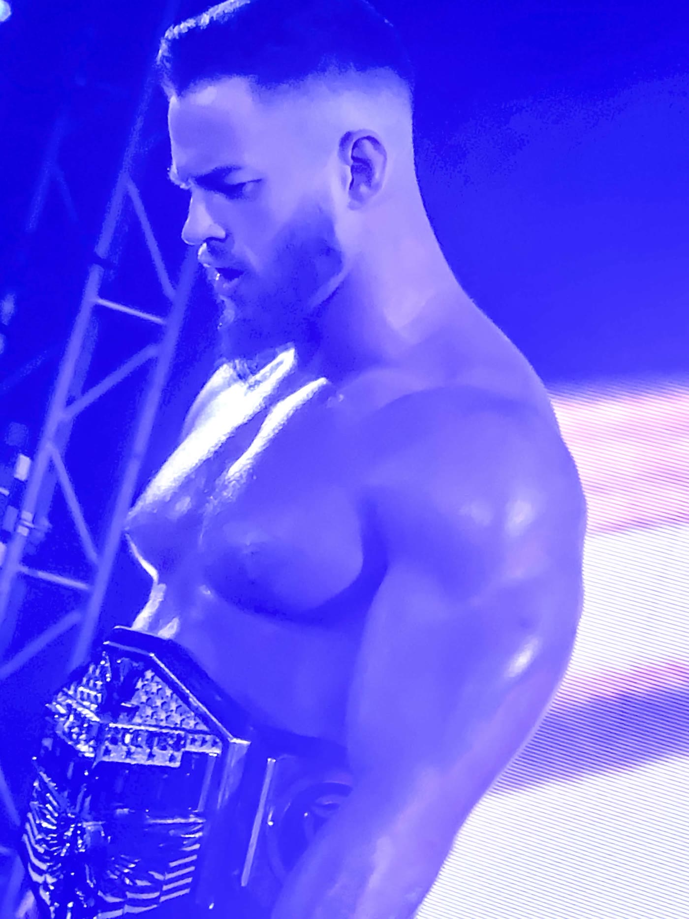 Wrestler in profile wearing a championship belt, lit hard in blue on the entrance ramp