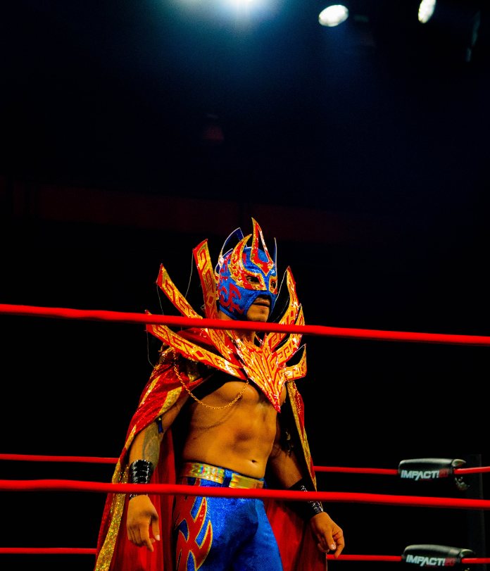 Masked luchador in an ornate red and blue entrance costume between the ring ropes