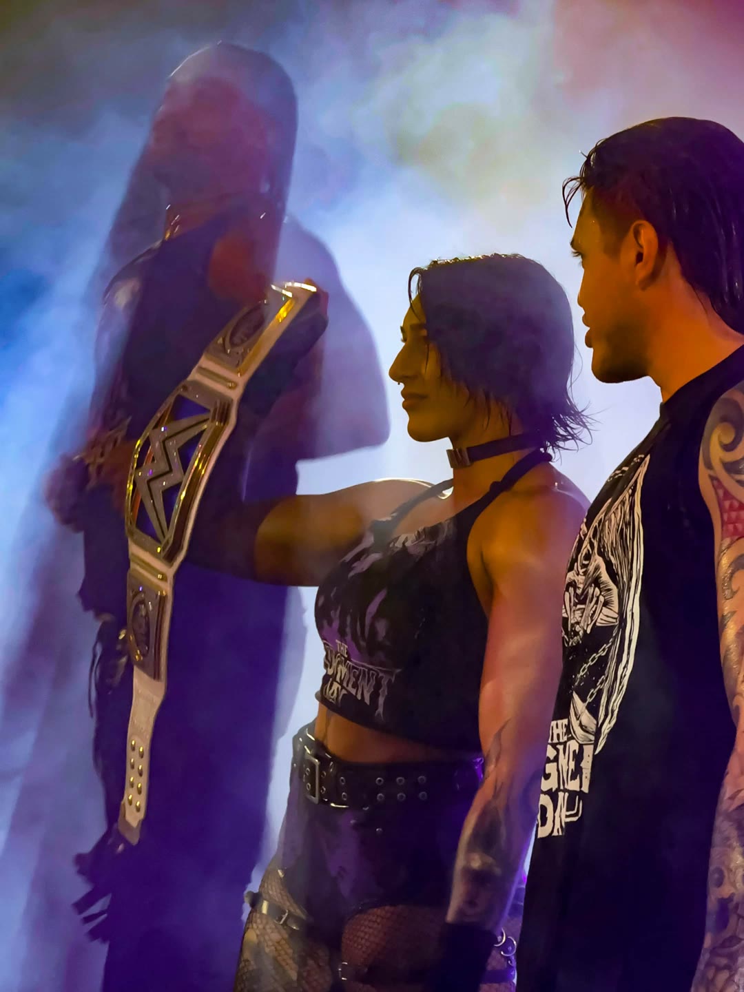 Two wrestlers in a smoke-lit entrance, one raising a championship belt overhead