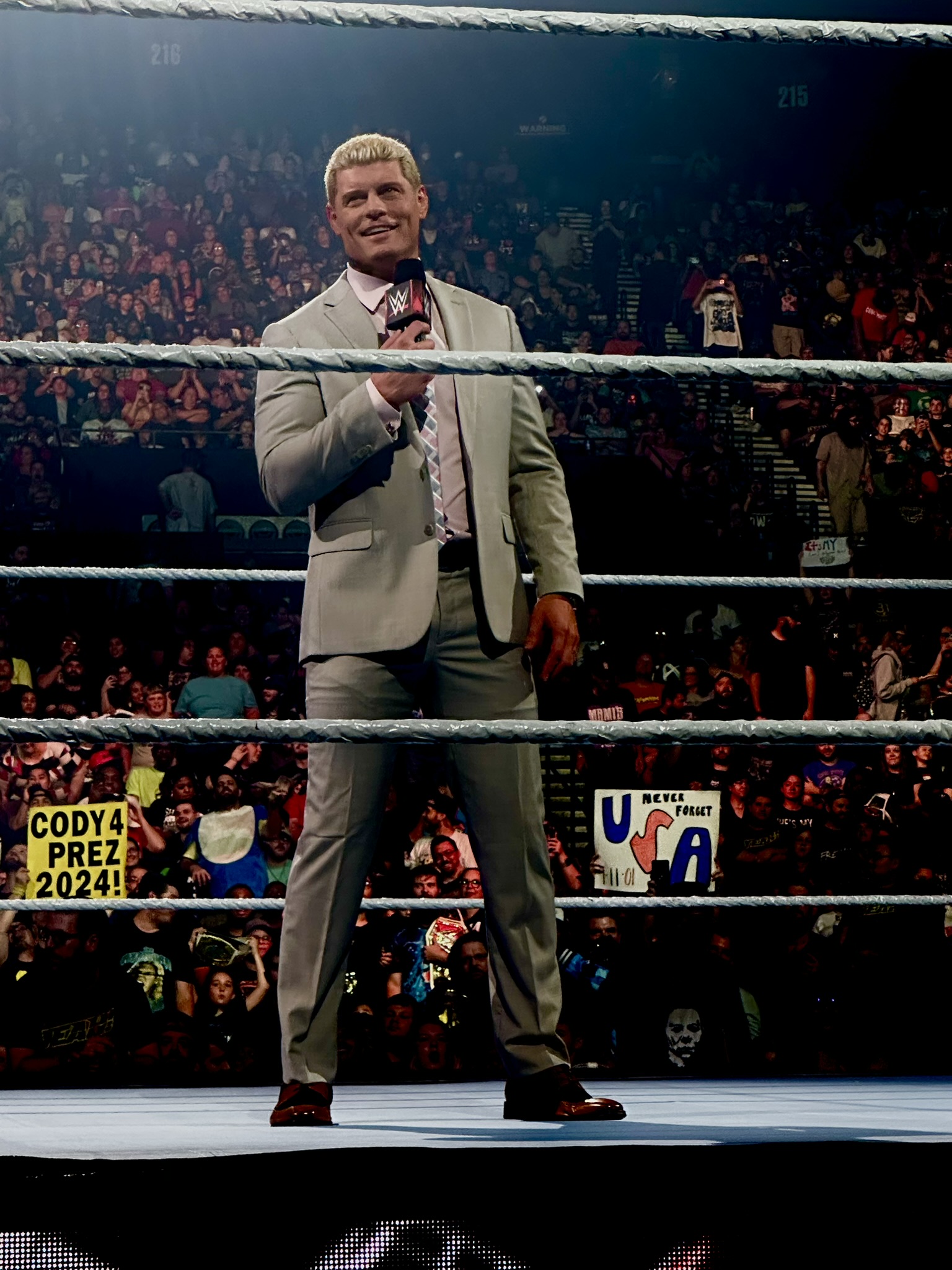 WWE wrestler in a suit holding a WWE-branded microphone in the ring
